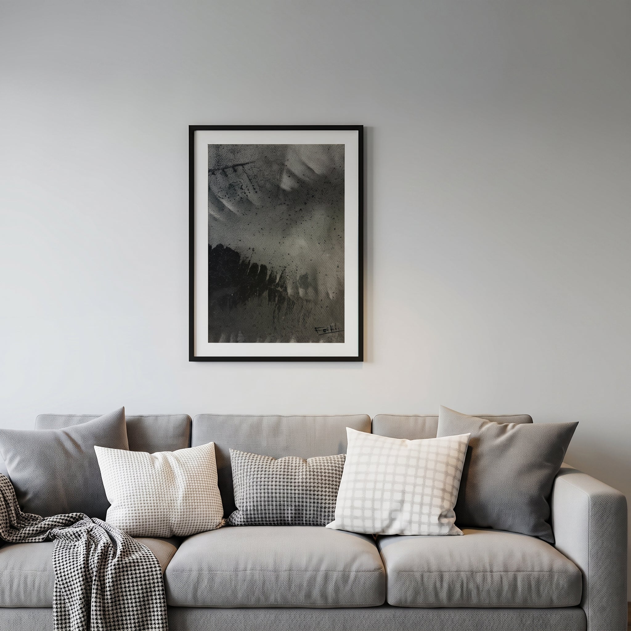 A framed abstract black and white art print entitled shadows of the past by feli the artist hangs on a light gray wall above a modern gray sofa with decorative throw pillows and a folded blanket.

