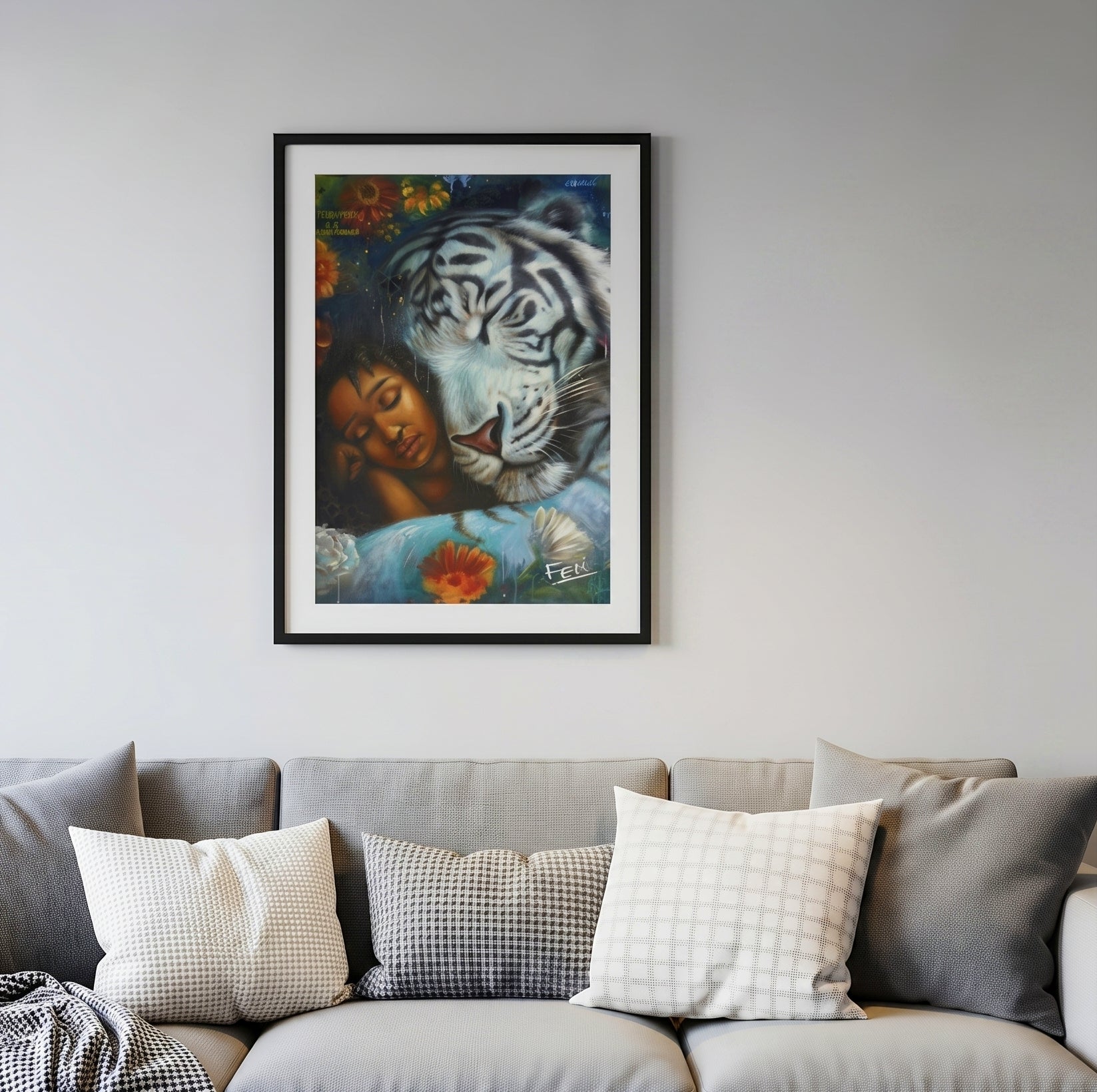 A framed art print entitled wild heart gentle soul by feli the artist depicting a woman resting peacefully with a large white tiger, in a black frame hung on a light gray wall above a modern gray sofa with decorative throw pillows.