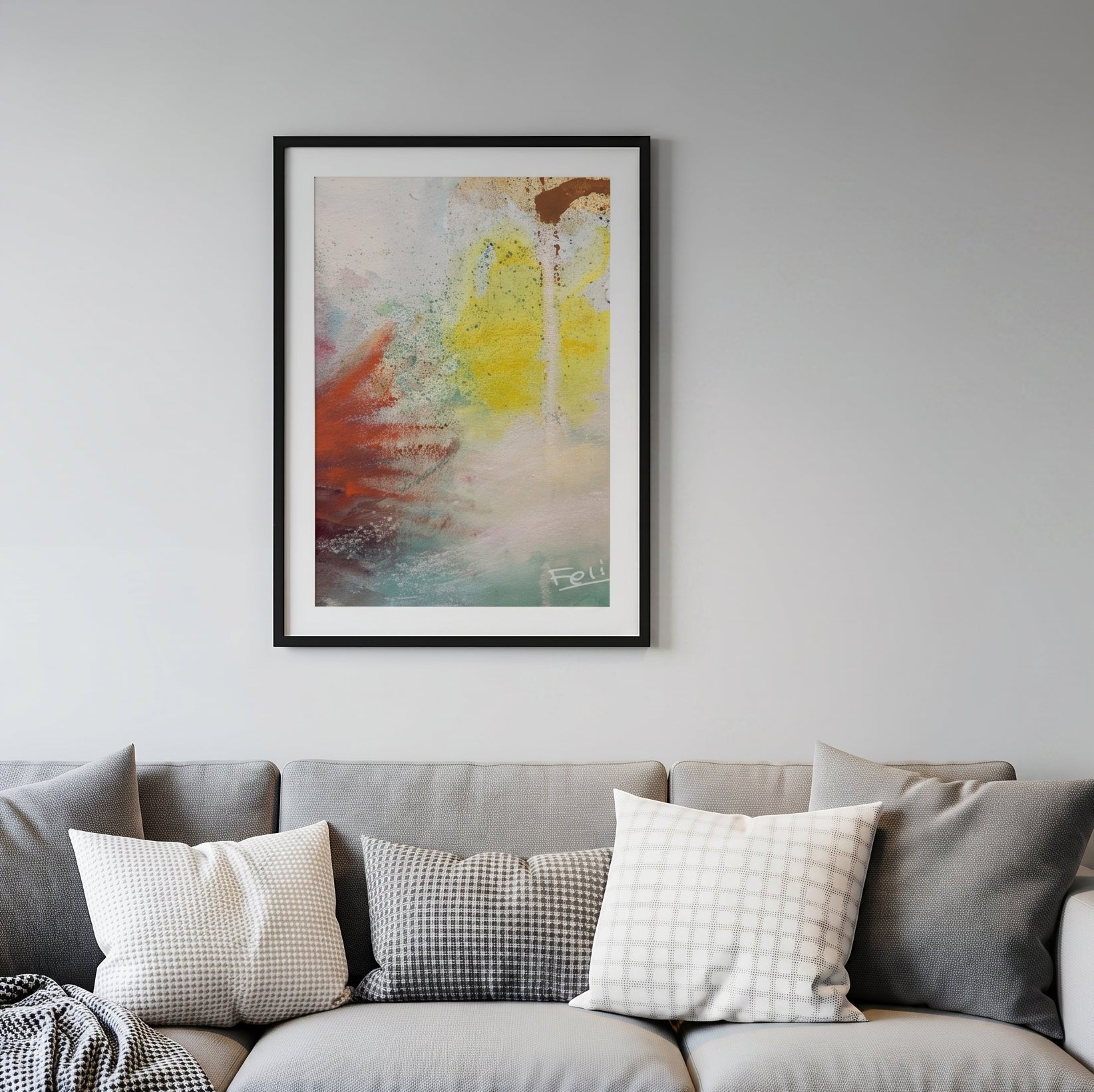 Touching the sky by feli the artist is a framed abstract art print featuring a textured composition of yellow, red, brown, and teal paint strokes on a white background hang in a black frame on a light grey wall above a grey sofa in the livingroom.