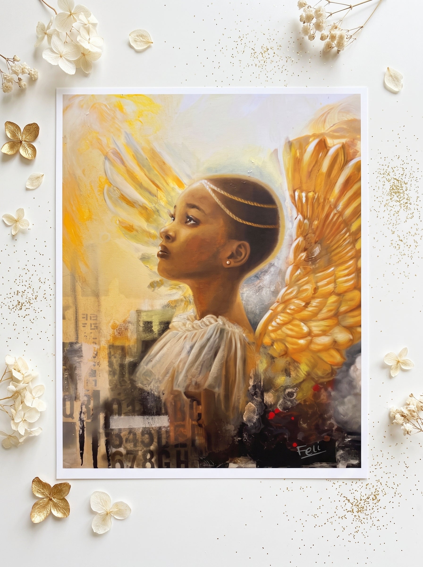 An art print entitled rays of hope by feli the artist featuring a stylized portrait of a black african girl with large golden angel wings, displayed on a white surface with scattered dried flowers and gold glitter accents.

