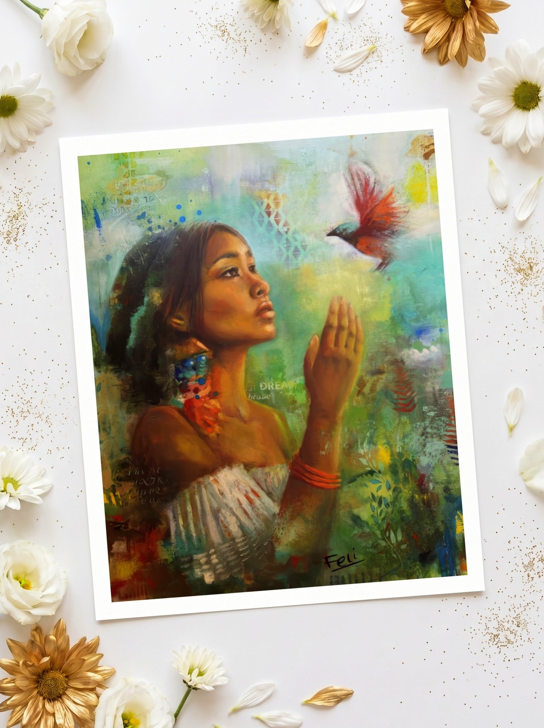 An art print entiled if i had wings by feli the artist featuring a green floral colorful portrait of a indian black mixed woman reaching for a hummingbird, styled flat-lay on a white surface with scattered white and gold flowers.