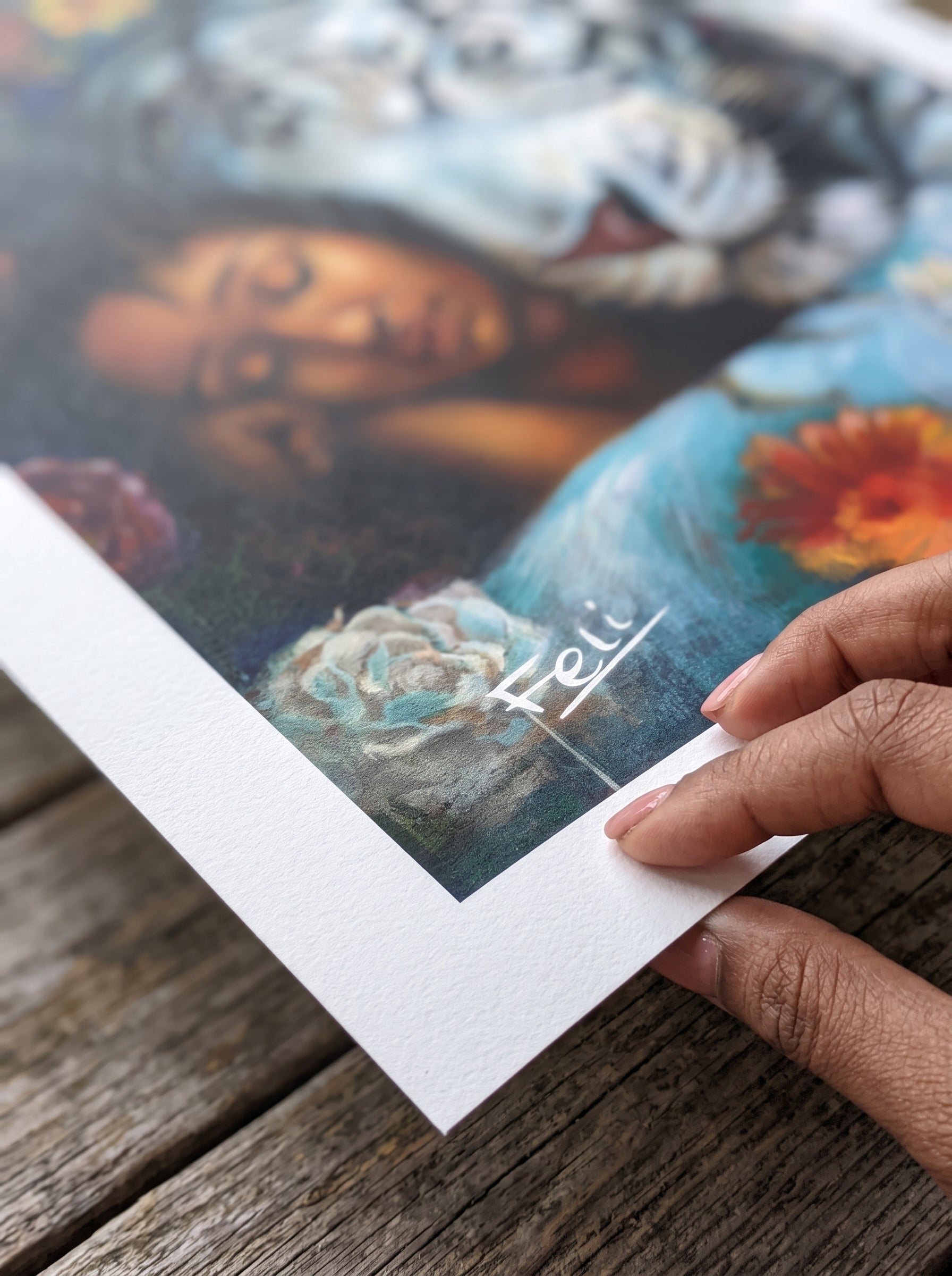 A close-up of a hand holding a printed art print entitled wild heart gentle sould by feli the artist. The artwork features a blue colored abstract realism painting with a woman's face, a white tiger, and floral elements.
