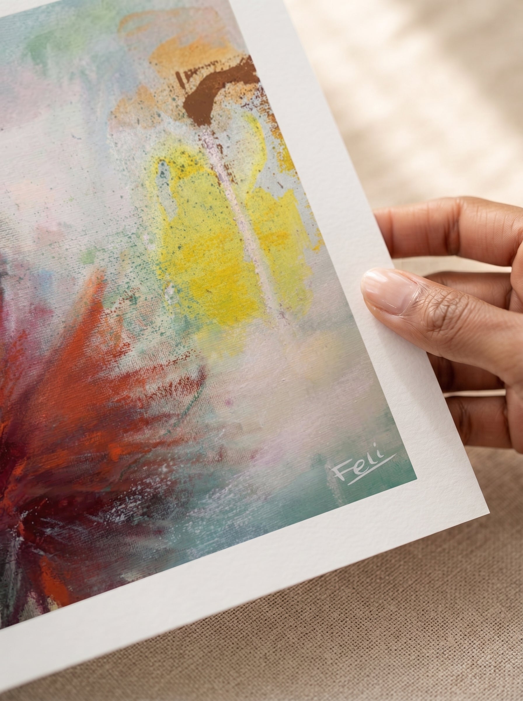 a hand holding the edge of an unframed art print titled Touching the sky by feli the artist which is An abstract art print featuring a textured composition of yellow, red, brown, and teal paint strokes on a white background.