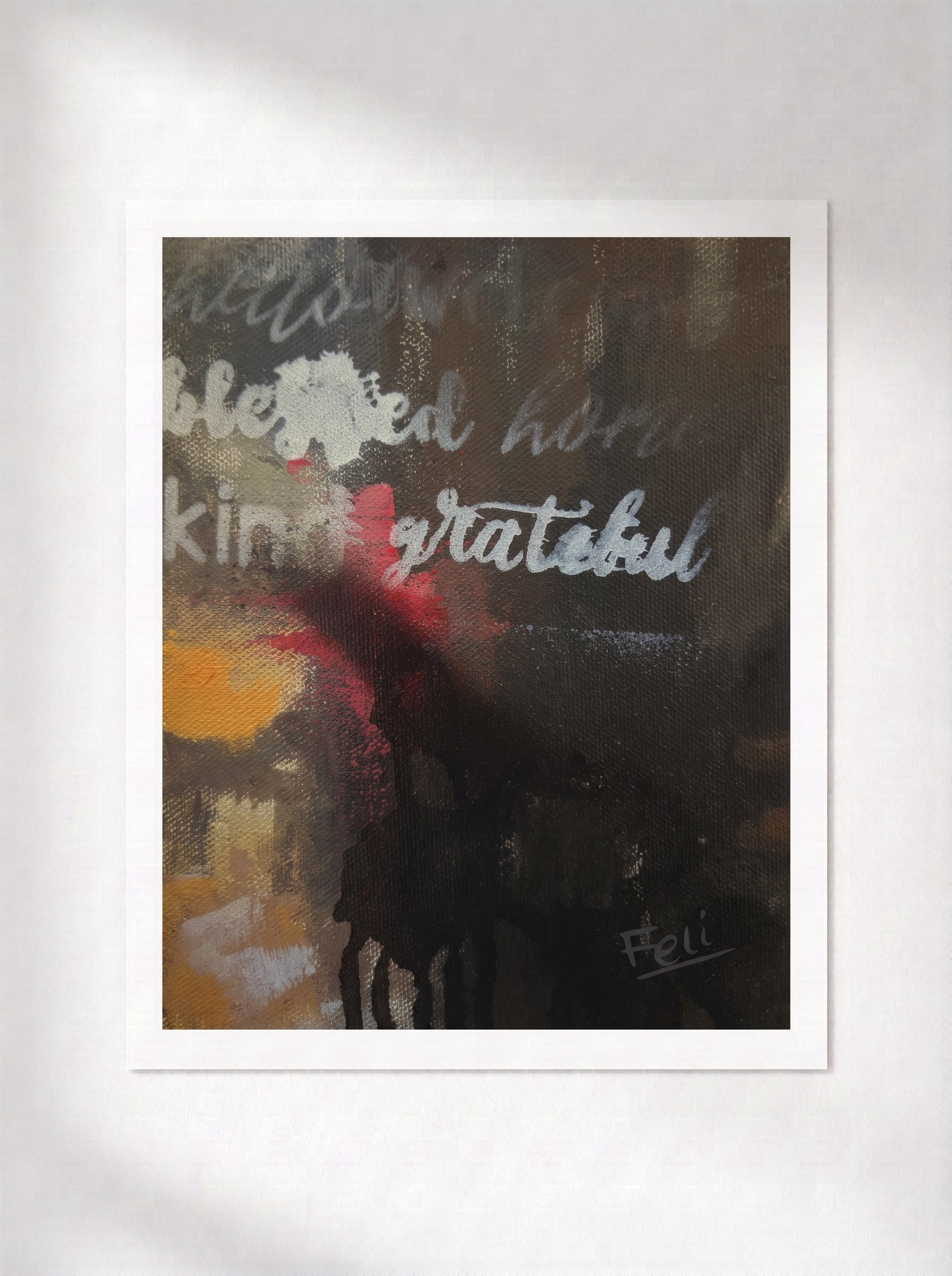 An unframed abstract art print titled grateful and blessed by feli the artist featuring the words 'blessed home', 'kind', and 'grateful' in white script over a dark, textured background with yellow and red accents, displayed on a light gray wall.