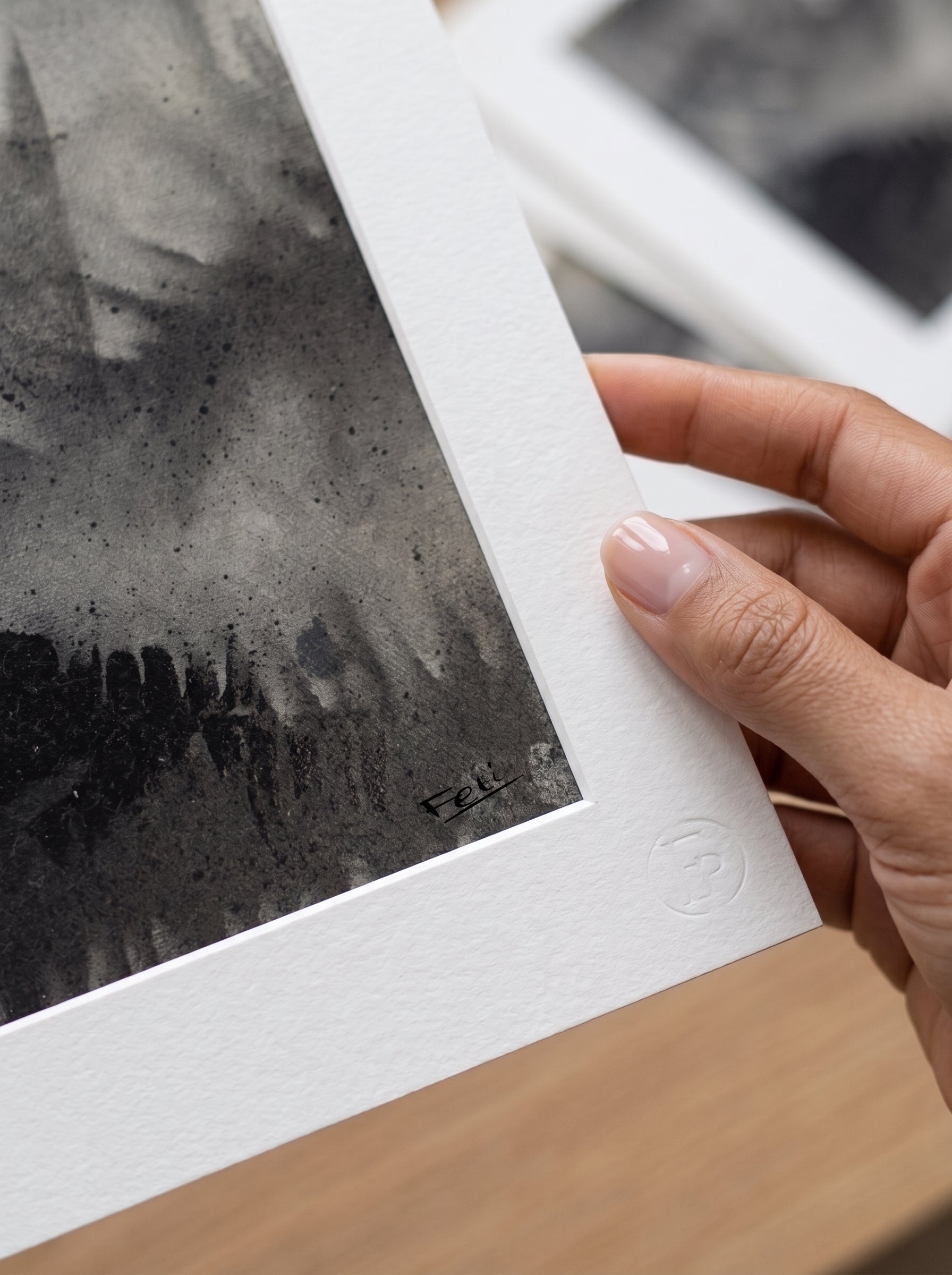 A close-up of a hand holding a matted art print with a black and gray abstract design entitled shadows of the past by feli the artist.