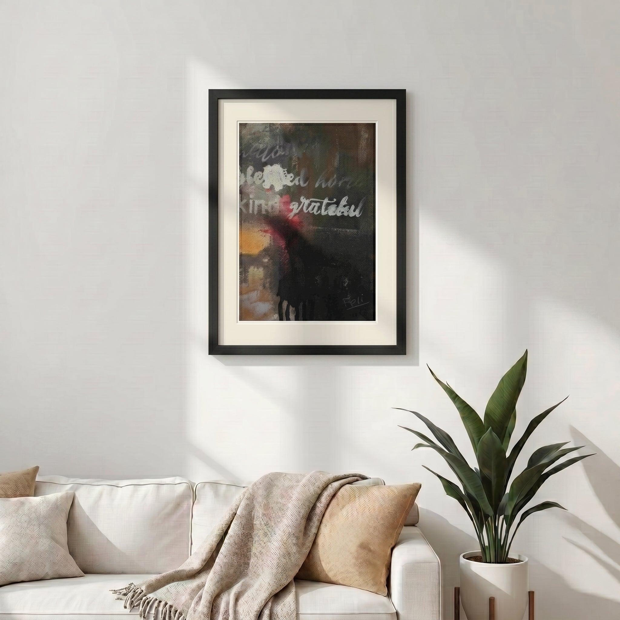 A framed abstract art print titled grateful and blessed by feli the artist featuring the words 'blessed', 'kind', and 'grateful' in white script over a dark, textured background with yellow and red accents, displayed in a black frame on a light gray wall hang in a modern livingroom.