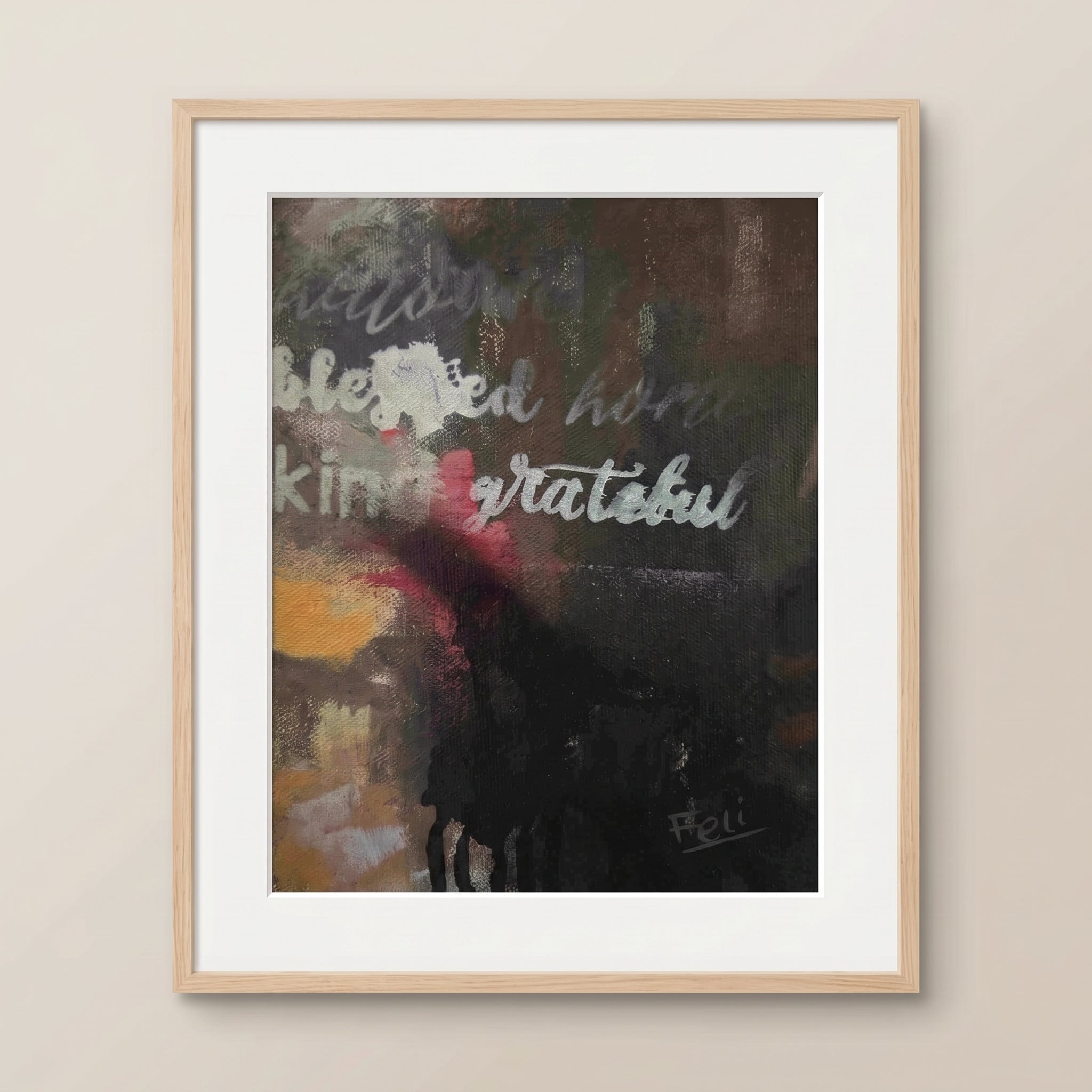 A framed abstract art print titled grateful and blessed by feli the artist featuring the words 'blessed', 'kind', and 'grateful' in white script over a dark, textured background with yellow and red accents, displayed in a natural wood frame on a beige wall.