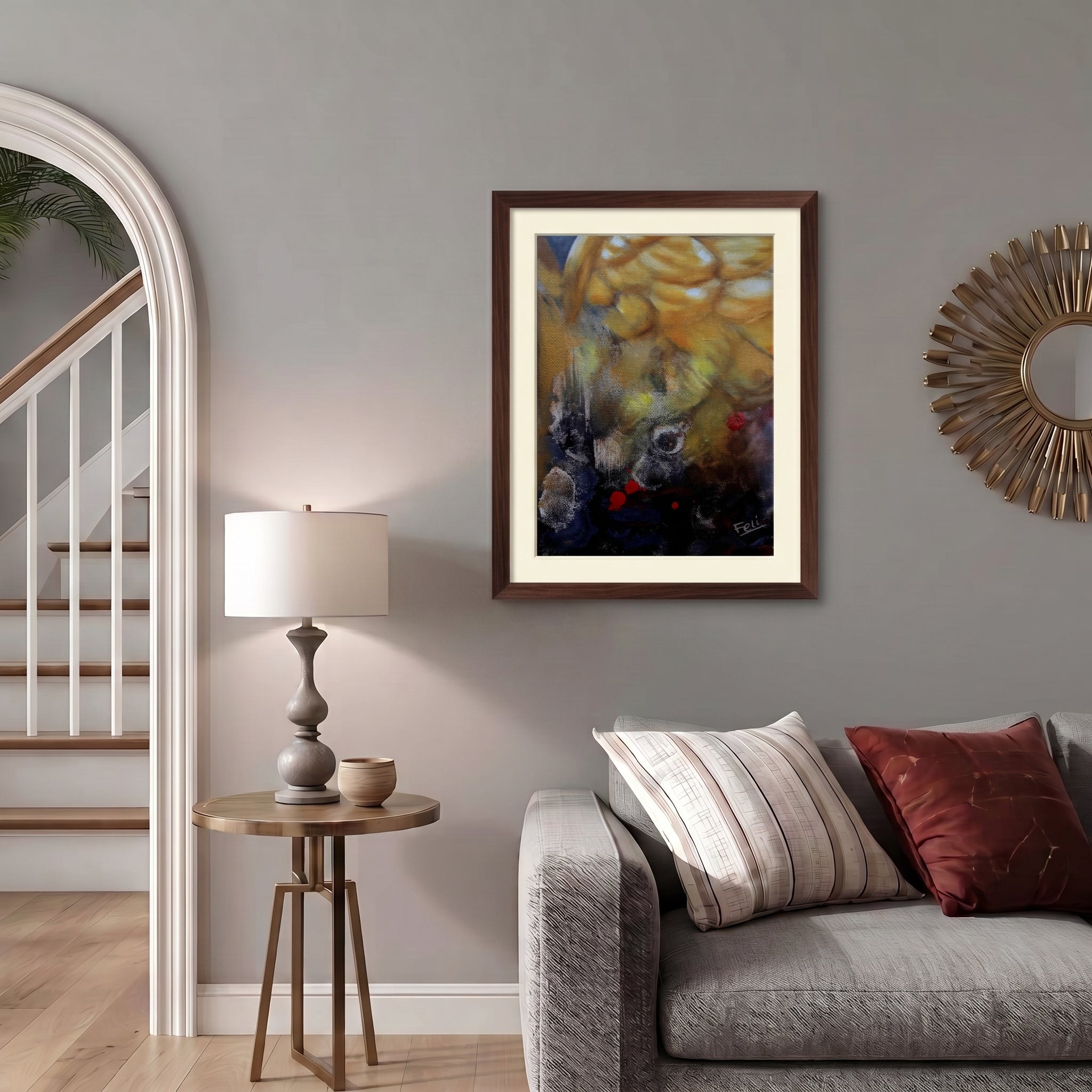 A framed abstract art print entitled my wings by feli the artist with yellow, gold, and dark blue tones displayed in a dark wood picture frame hang on a gray wall in a styled living room setting with a sofa, side table and lamp.