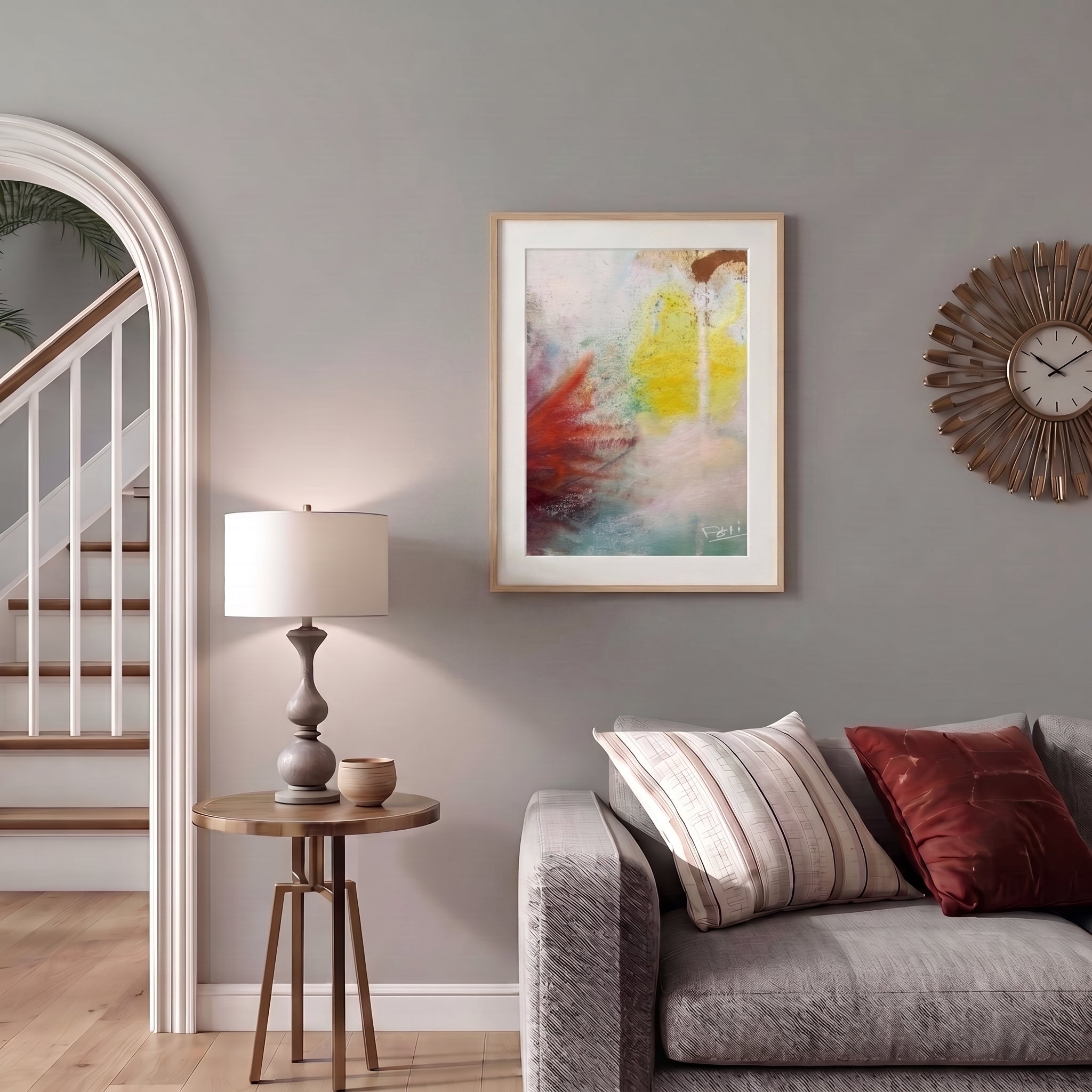 Touching the sky by feli the artist is A framed art print abstract and featuring a textured composition of yellow, red, brown, and teal paint strokes on a white background displayed in a natural wood picture frame hang on a light grey wall above a grey sofa in a colorful livingroom.