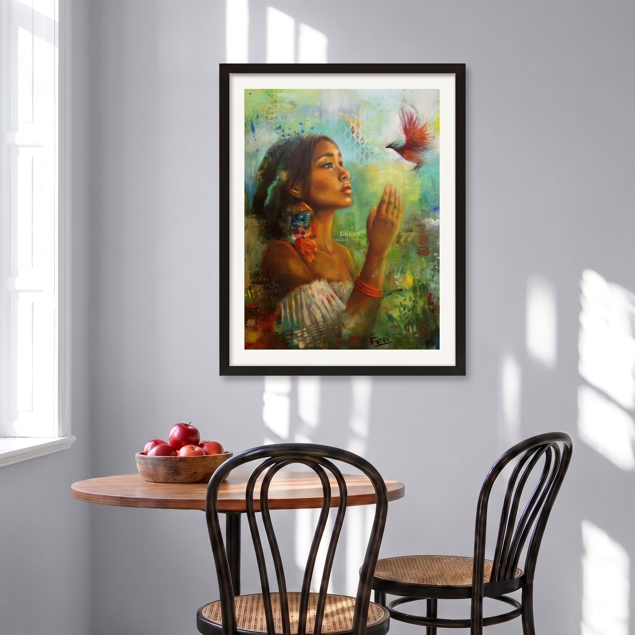 A framed art print entitled if i had wings by feli the artist featuring a colorful painting of a woman with a bird, displayed in a black frame on a light gray wall above a wooden dining table and chairs.