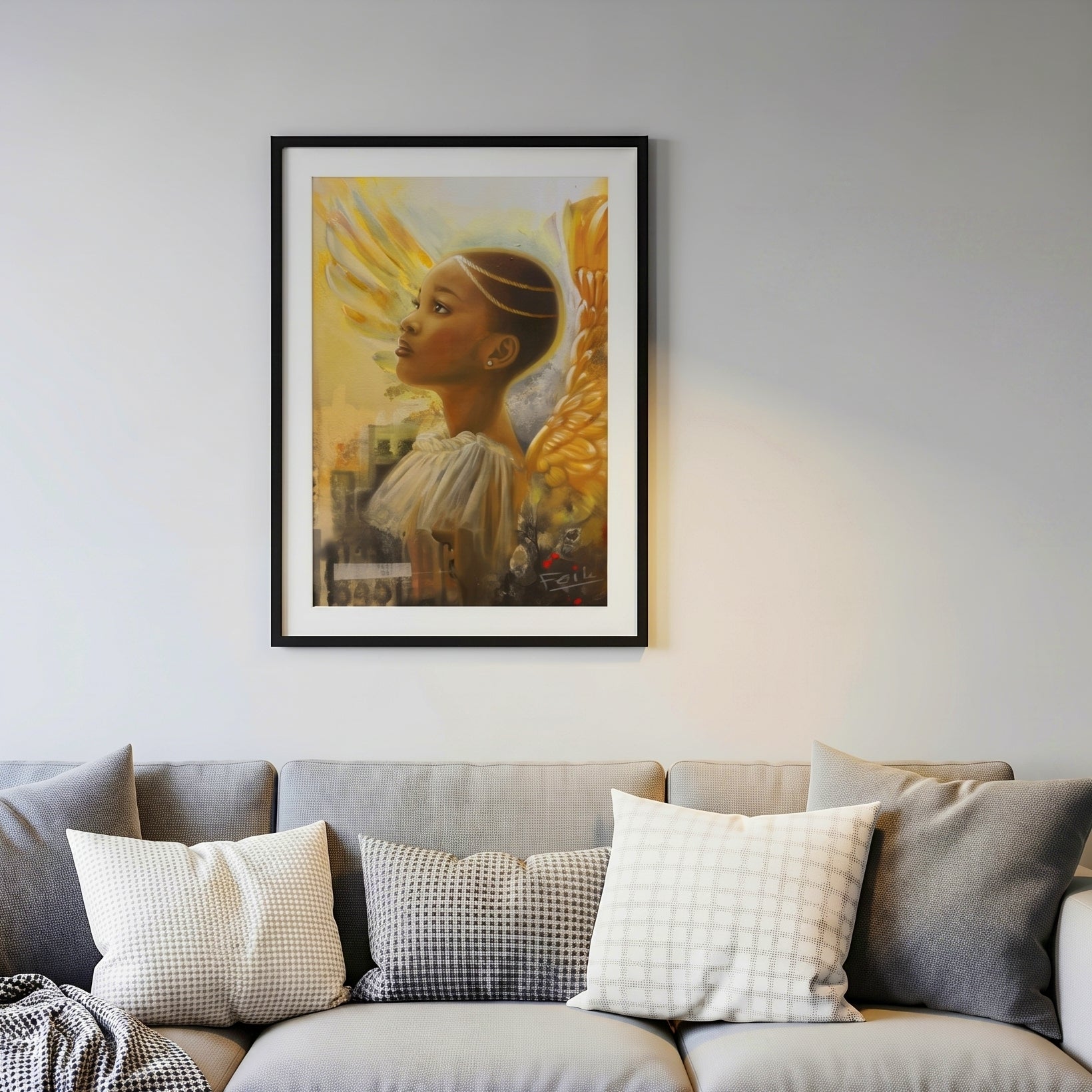 A framed art print entitled rays of hope depicting a young Black african angel with golden wings displayed in a black picture frame hanging on a light gray wall above a modern gray sofa with patterned throw pillows.